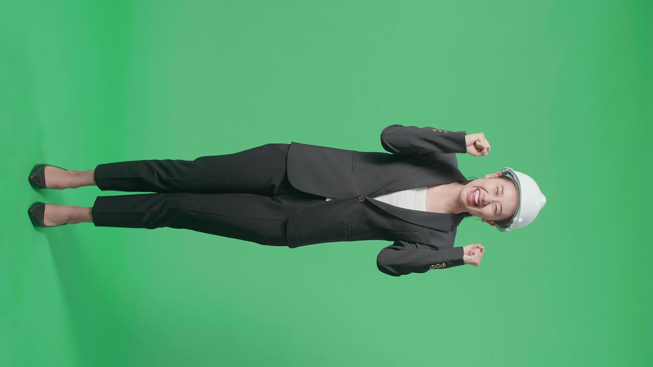 Full Body Of Happy Asian Female Engineer With Safety Helmet Celebrating While Standing On Green Screen In The Studio