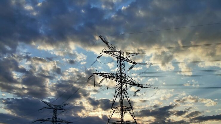 Majestic silhouette of high voltage electrical towers and power lines against a beautiful, cloudy sky during a colorful sunset