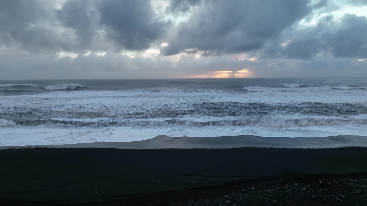 Aerial landscape view of ocean waves crashing on Iceland S&oacute;lheimasandur black sand beach, on a cloudy sunset