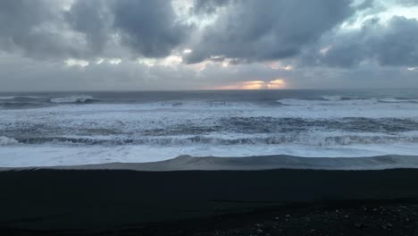Aerial-landscape-view-of-ocean-waves-crashing-on-Iceland-Sólheimasandur-black-sand-beach,-on-a-cloudy-sunset