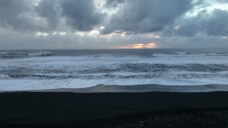 Vista-Aérea-Del-Paisaje-De-Las-Olas-Del-Océano-Rompiendo-En-La-Playa-De-Arena-Negra-De-Sólheimasandur-En-Islandia,-En-Una-Puesta-De-Sol-Nublada