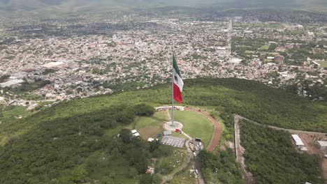 aerial drone fast moving shot of large majestic red, white and green mexican flag waving in wind along hilly terrain at daytime