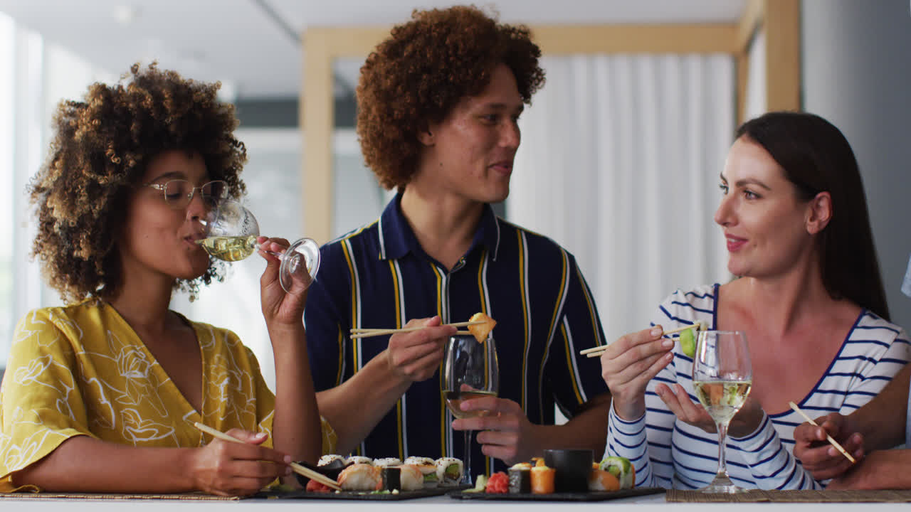 Diverse group of happy friends drinking wine eating sushi and talking at a bar