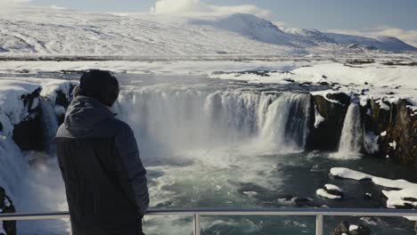 tourist stand near metal safety barrier at panoramic godafoss waterfall