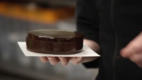 close-up of a person decorating a shiny chocolate cake on a plate, in a kitchen