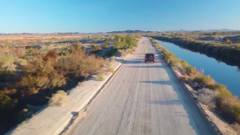 Vista-Aérea-De-Seguir-Un-Todoterreno-Conduciendo-Por-Una-Carretera-Cerca-Del-Canal-De-Riego-Por-Gravedad-De-Gila---Yuma,-Arizona