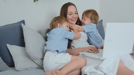 Mamá-Está-Sentada-En-El-Sofá-Con-Una-Computadora-Portátil.-Dos-Niños-Cantan-Y-Besan-A-Su-Mamá.