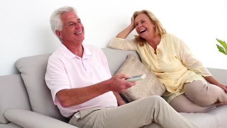 retired smiling couple watching television on the couch