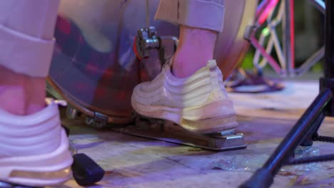 a close up image of a drummer's foot beating a drum with a pedal. white sneakers used by drummers are seen moving the bass pedal. music video. no face video