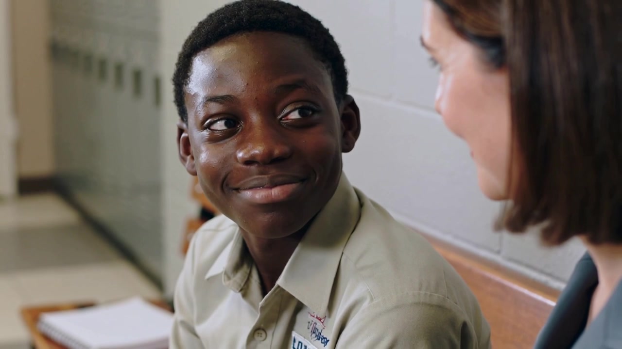 Placing hand and speaking staff comforting teen on hallway bench khaki nametag blazer, teen smiling