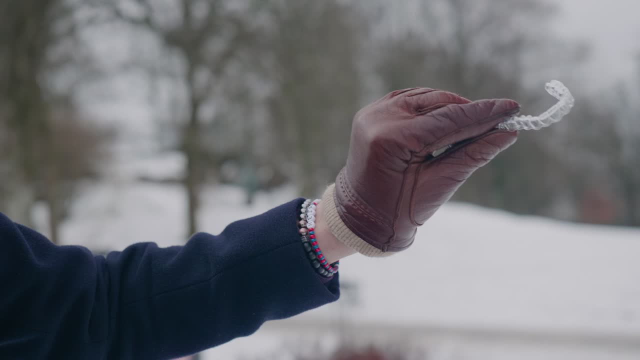 Hand showcasing a clear aligner for teeth regulation, winter day, close up shallow depth of field