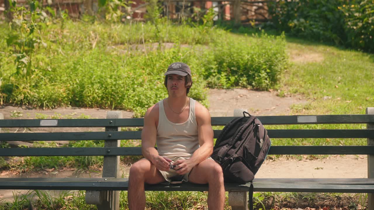 갈색  ⁇ 탑을 입은 젊은 남자가 선글라스를 벗고 얼굴에서  ⁇ 을  ⁇ 고 일어납니다.