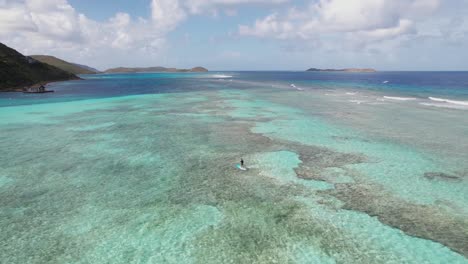 aerial view of person on paddle board in caribbean sea water floating above coral reef, drone shot