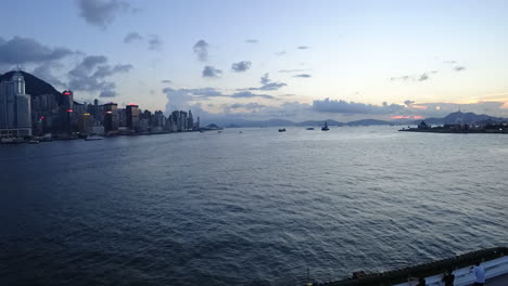 china,hong kong harbor's time lapse during sunset, clouds and ships moving in and out, lights start to turn on one by one.