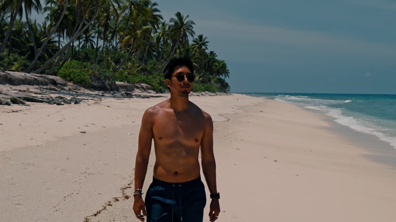 A solitary man walks along the untouched shoreline of Geiymiskih Fannu Beach in Fuvahmulah, surrounded by swaying palm trees and the gentle rhythm of turquoise waves.
