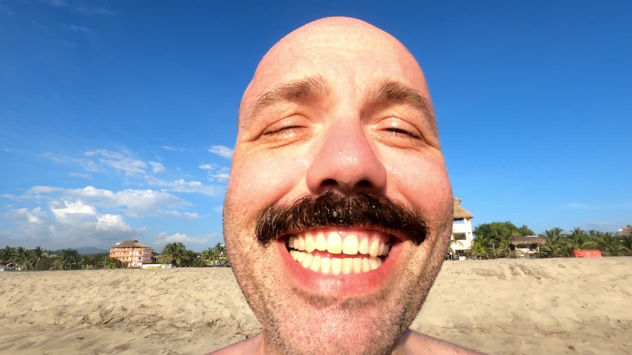 retrato de un hombre calvo caucásico con bigote sonriendo desde la cámara mientras disfruta de sus vacaciones de verano en la playa del océano