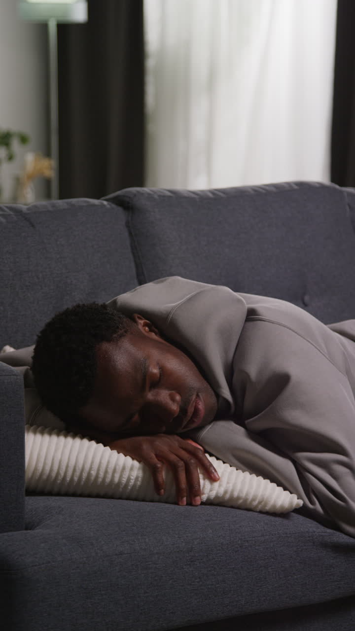Vertical Video Of Unhappy And Depressed Young Man Lying On Sofa At Home Looking Anxious And Worried