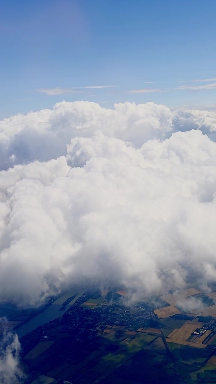 Aerial view flying above thick white clouds revealing farmland and fields below