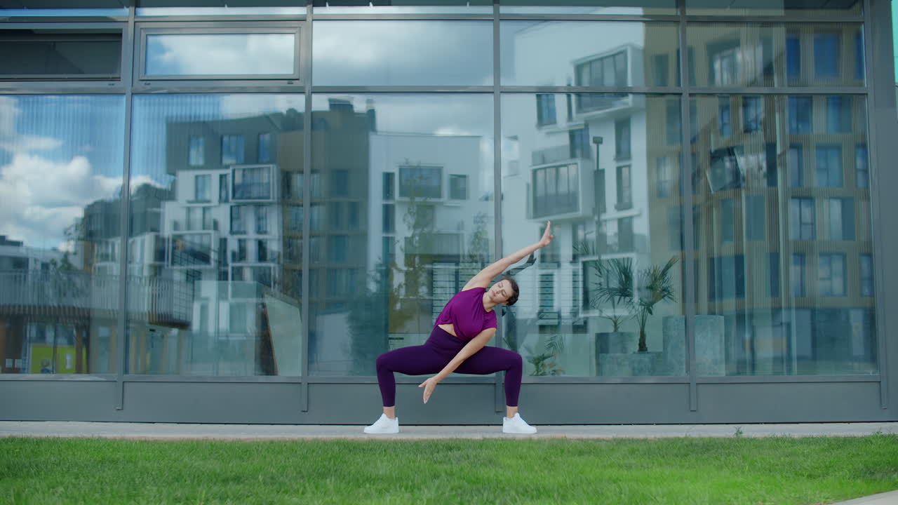 Woman doing yoga poses outdoors in front of a modern building
