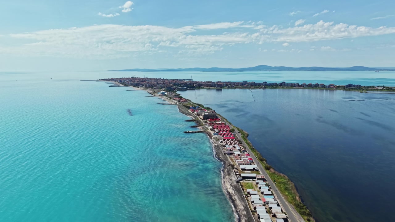 Yazın gündüz vakti, uzakta bir yerleşim yeri ile kara ve okyanusu gösteren berrak su ve sahil şeridi manzarası.