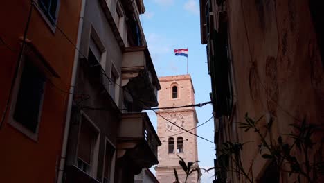 A-street-in-the-city-of-Sibenik,-with-the-Croatian-flag-in-the-background