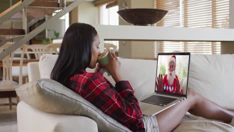 mixed race woman on laptop video chat having coffee during christmas at home