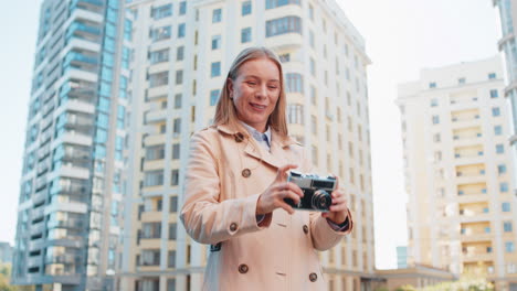 mujer adulta feliz turista explorando la ciudad haciendo fotos en cámara retro vintage en la calle de la ciudad