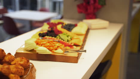 muffins pastries fruits crackers cheese on wooden board platters on white countertop with tables and chairs in background