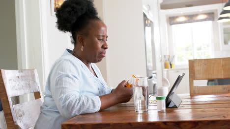 African-american-senior-woman-having-video-call-and-holding-medicines-in-sunny-room,-slow-motion