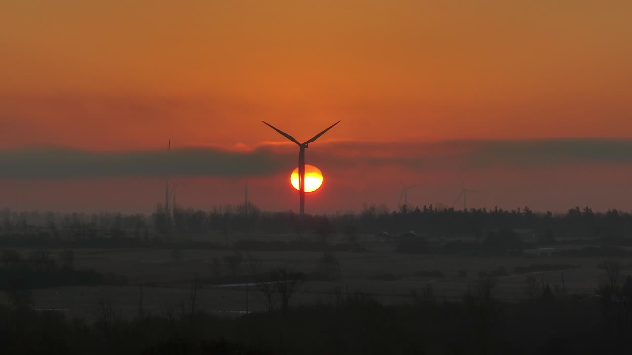 일출 동안 뒤에 태양이 있는 회전하는 풍차의 공중 클로즈업