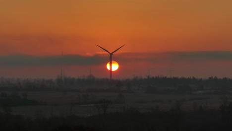 aerial close up of a turning windmill with sun in behind during sunrise