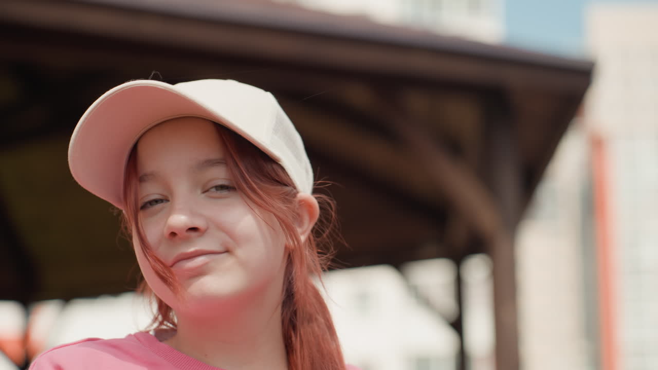 White Teenage Girl Wearing Cap Smiling, Sunlit Wooden Pavilion Background, Candid Closeup With Red Hair Ponytail, Soft Warm Tones, Natural Freckles, Relaxed Expression And Influencer Lifestyle Vibe