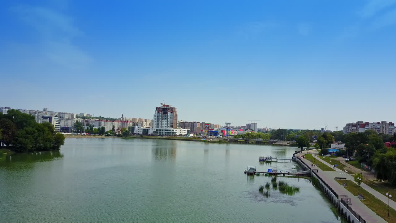 Flying above the river floating through the modern city. Lively traffic by the roads at waterfront among the multi-storied buildings. Top view.