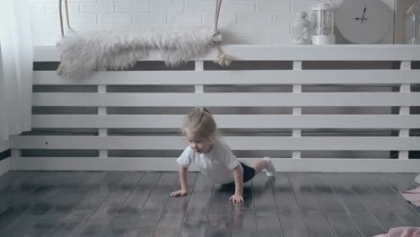 cute toddler pushes up on wooden floor against wall shelf