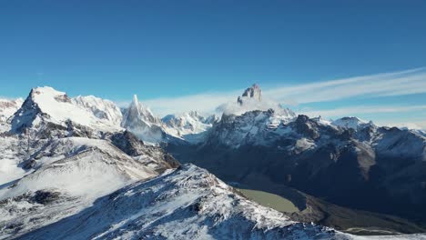 drone panorama over laguna torre near el chaltén. majestic fitz roy and cerro torre peaks stand snow-covered beneath a cloudless sky in patagonia’s rugged andes