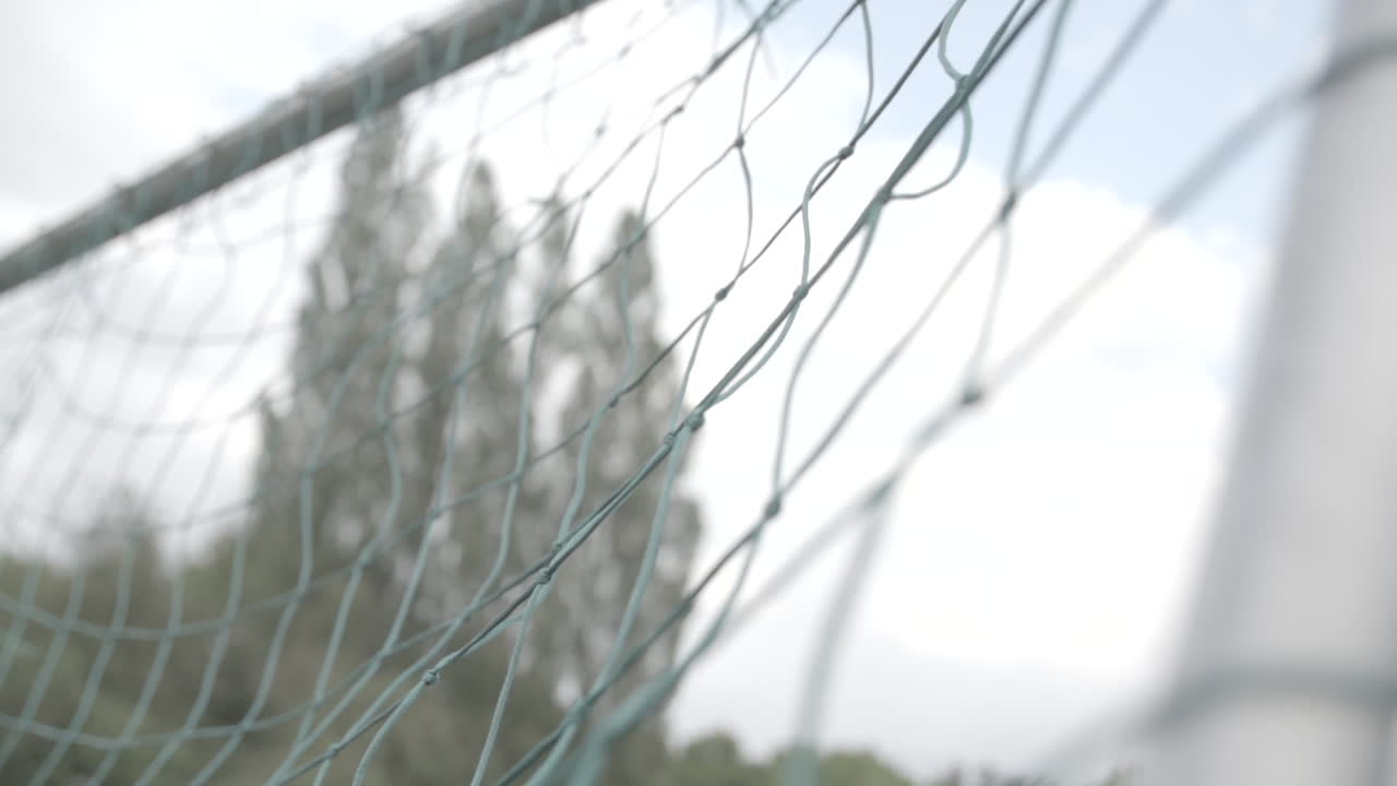 Close up slowmotion shot of a football flying into the green net of a goal on a cloudy day LOG