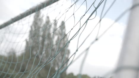 close up slowmotion shot of a football flying into the green net of a goal on a cloudy day log