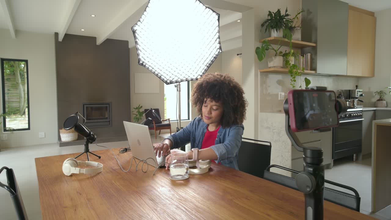 Vlogueuse entrant dans la cuisine, ajustant trépied et éclairage, tapant sur un ordinateur portable et enregistrant, avec espace de copie.