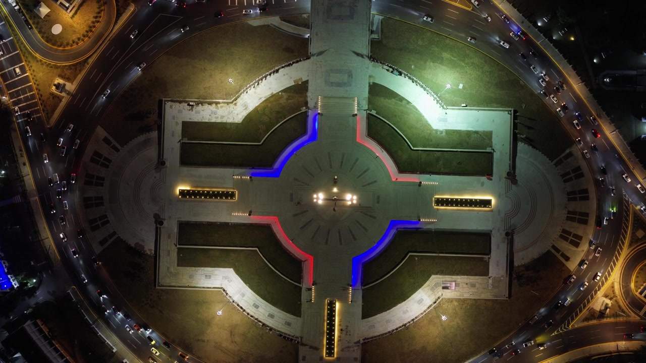 Vista drone direttamente sopra il monumento illuminato di Plaza de la Bandera e il traffico della rotonda di notte a Santo Domingo. Ripresa aerea dall'alto in discesa
