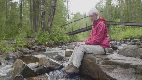 mujer sentada junto a un río en un bosque