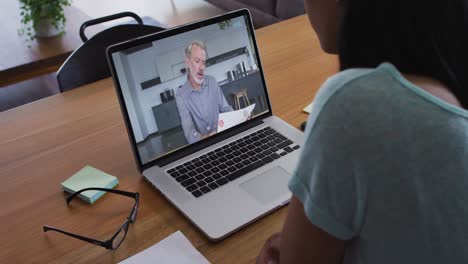 Mixed-race-businesswoman-sitting-at-desk-using-laptop-having-video-call-with-male-colleague