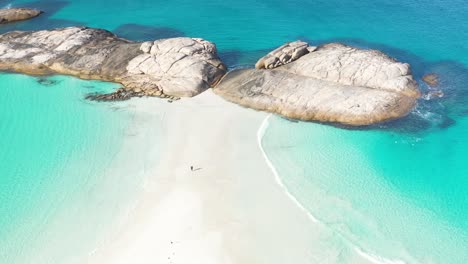 Excelente-Toma-Aérea-De-Un-Turista-Parado-Entre-Arena-Blanca-Y-Surf-Azul-Claro-En-Wylie-Bay,-Esperance,-Australia