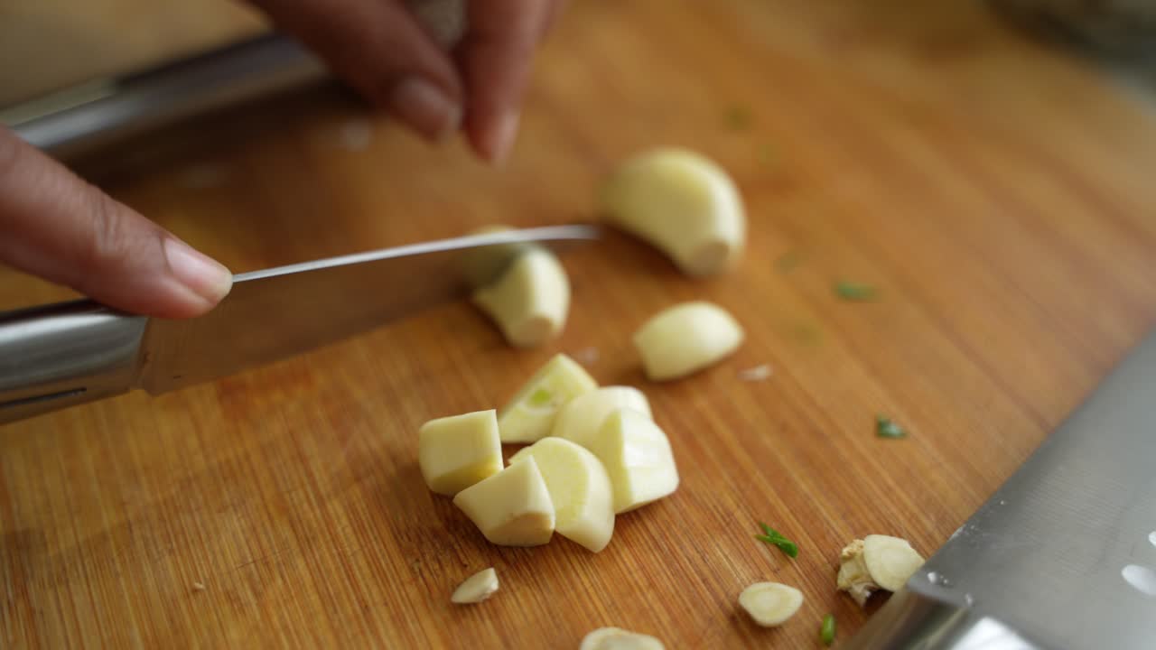 Closeup shot of chef slicing garlic cloves into pieces on chopping board.