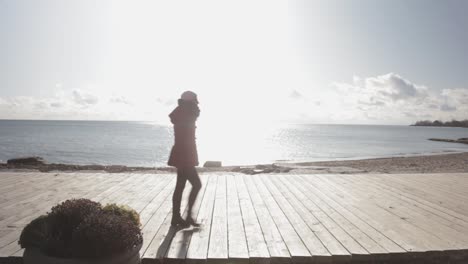 Una-Mujer-Caminando-A-Lo-Largo-De-La-Orilla-Del-Lago-Con-La-Hermosa-Luz-Del-Sol-De-La-Mañana-Brillando-Más-Allá-De-La-Superficie-Del-Agua---Plano-Medio