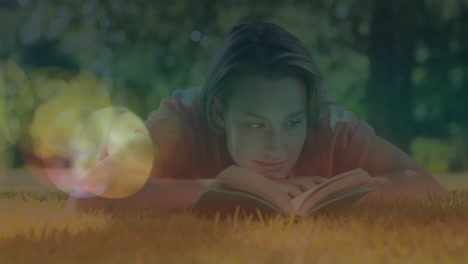 animation of lights over caucasian woman lying on lawn and relaxing with book