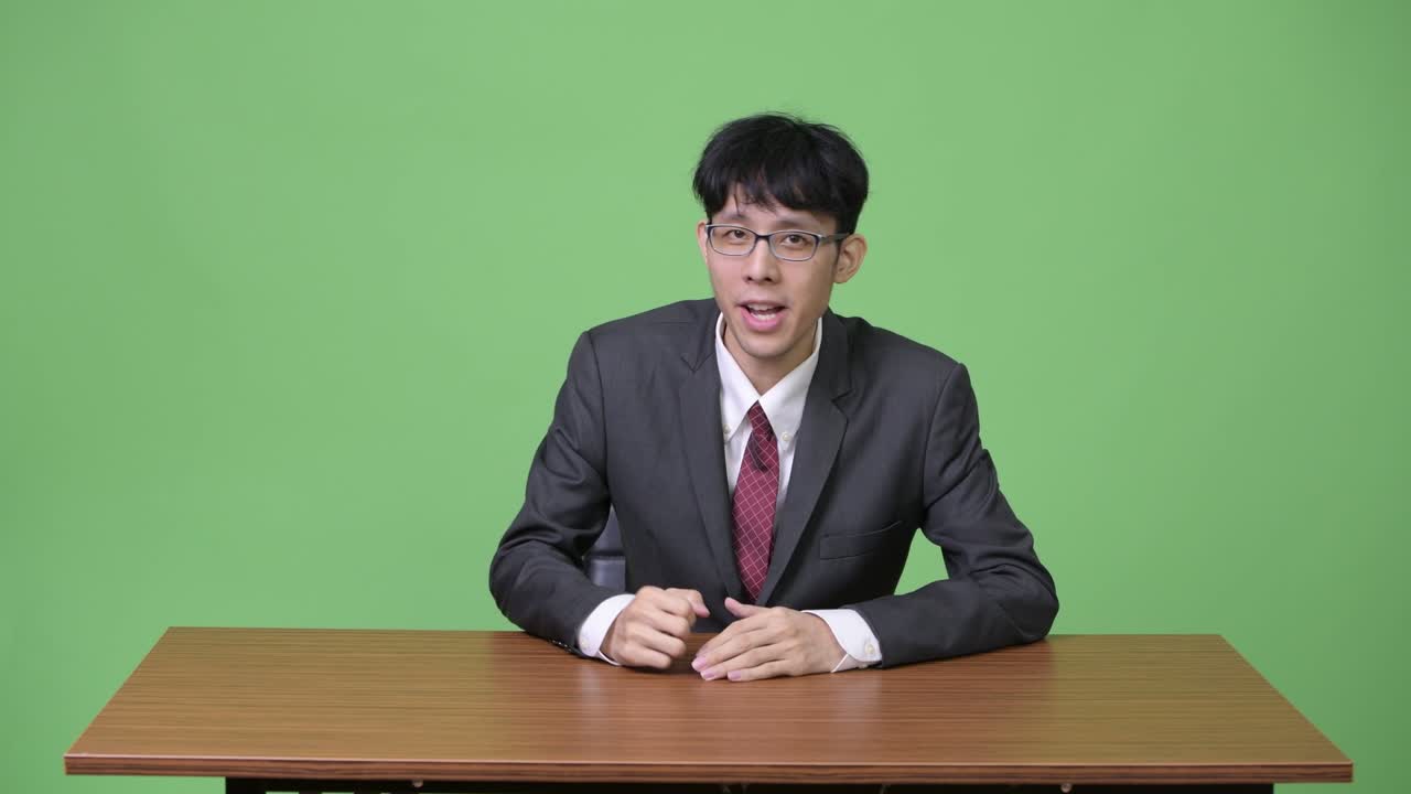 젊은 아시아 사업가 뉴스 캐스터로 이야기하고 뒤에서 무언가를 제시