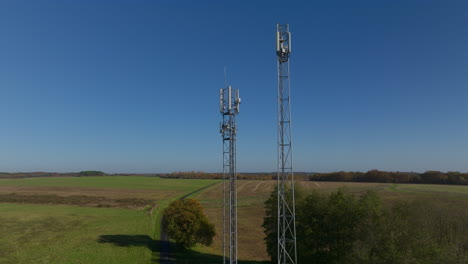 two cellular towers in the middle of farmland during sunrise, aerial dolly up tilting