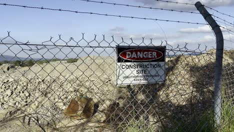 close up shot of a danger construction site sign on a barbed wire fence, pile of dirt in background.
