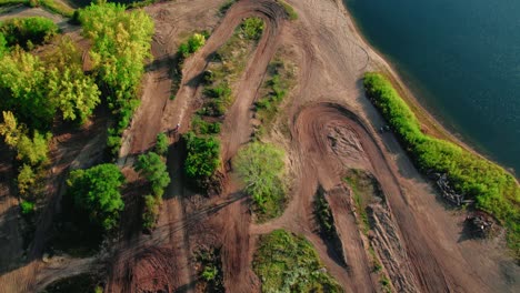 Epische-Eröffnungsszene-Eines-Motocross-Fahrers-Auf-Einem-Dirtbike,-Der-Abseits-Von-Straßen-Durch-Einen-Wald-Neben-Einem-See-Fährt