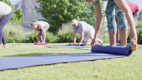 diverse group of male and female seniors rolling up yoga mats after exercise in garden, slow motion